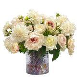 Elegant café au lait floral arrangement with ranunculus peonies roses dahlias and anemones displayed in a decorative cut glass vase.
