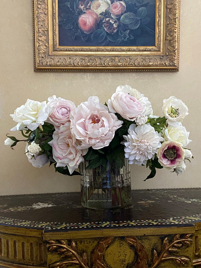 A realistic cream-colored faux rose and ranunculus tabletop arrangement in clear cut glass vase