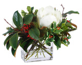 Hand-crafted magnolia, red berries, and greenery in a square glass vase, displayed against a white background