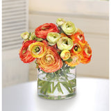 Luxury faux ranunculus centerpiece with orange, coral, gold, and soft green blooms arranged in a clear glass vase