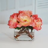 Salmon pink faux peony arrangement displayed in a modern clear square glass vase