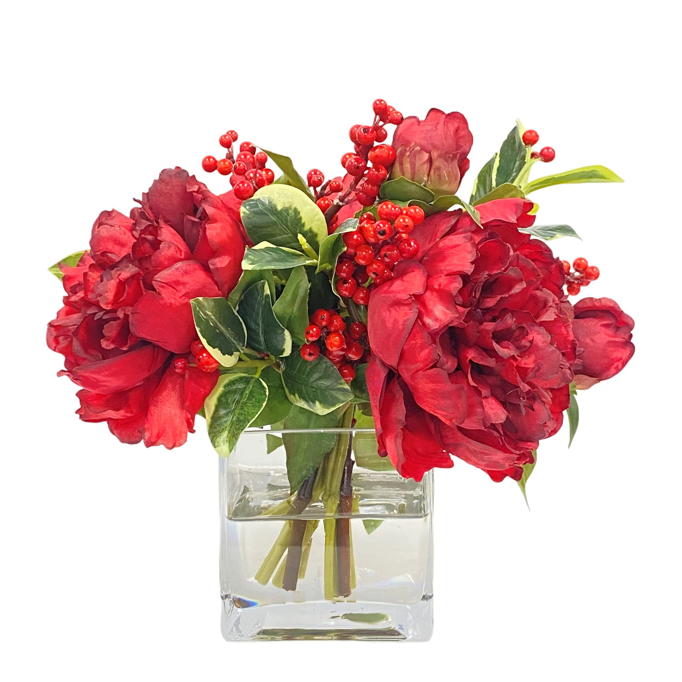 Red peony floral arrangement with green foliage in a glass cube vase, against a white background