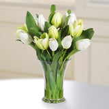 Realistic white faux tulip arrangement in a clear flared glass vase with lush green foliage